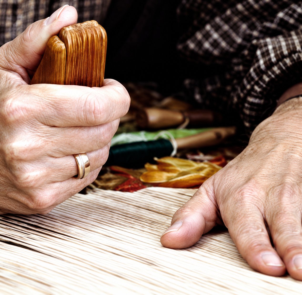 Gros plan sur les mains d'un artisan qui travaille des fils tendus sur un métier à tisser, une bague au doigt.